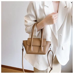 Detail of camel lychee grain leather bucket bag held by a model in a white blazer