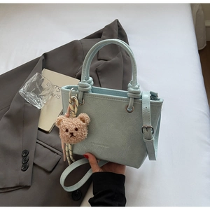 Detail of light blue wrinkled texture bucket bag with plush bear charm and long strap
