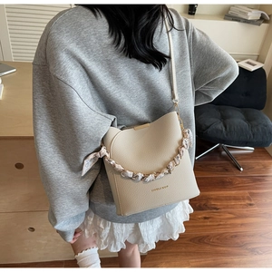 Detail of beige lychee textured bucket bag with silk scarf handle and golden logo