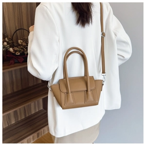 Brown litchi grain bucket bag with cat ear shape worn crossbody on white blazer
