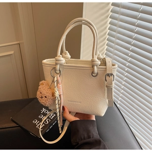 Detail of white pleated PU bucket bag with bear charm and adjustable shoulder strap