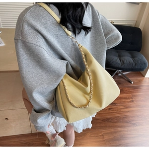 Close-up of a pale yellow pebbled leather hobo bag with gold chain strap on a model