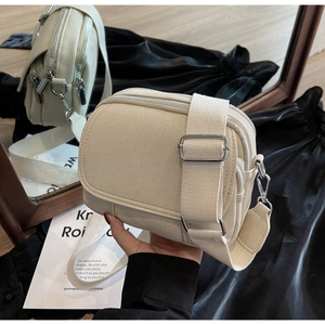 Detail van beige crossbodytas met meerdere vakken, brede riem en zilveren metalen gespen