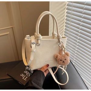 Detail of off-white bucket bag with bear charm, knot handles and branded logo imprint