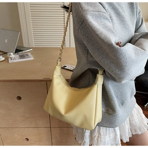 Close-up of yellow pebbled leather hobo bag with gold chain strap on a shoulder