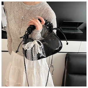 Détail du sac croissant noir avec poignée plissée, chaîne de perles et nœud en dentelle