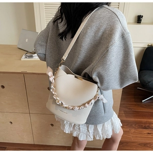 Détail du sac seau crème avec texture litchi, chaîne dorée et foulard en soie décoratif