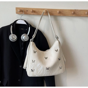 Detail of butterfly-buckle cream leather underarm bag with pleated texture on a wooden hook