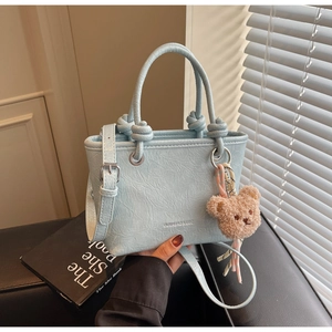 Close-up of light blue textured leather tote with knot handles and cute bear charm