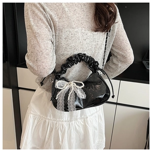 Détail du sac croissant en cuir verni noir avec nœud en dentelle blanche et perles