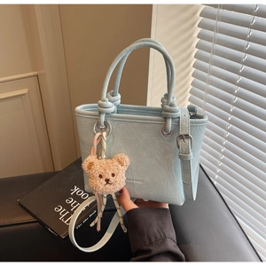 Close-up of pleated sky blue bucket bag with beige plush bear charm and thin strap