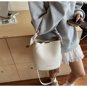 Détail du sac seau crème avec texture grainée et poignée décorée d'un foulard