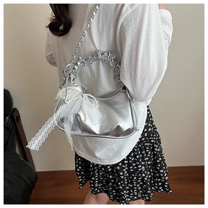 Détail du sac croissant argenté avec nœud en dentelle et breloque en perles
