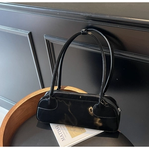 Close-up of minimalist black patent leather baguette bag on a dark wooden seat