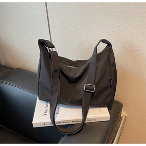 Detail of black nylon crossbody bag with adjustable strap and brand logo on a white book