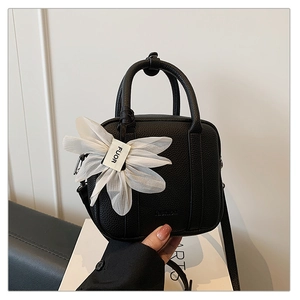 Close-up of black Boston bag with pebbled leather texture and white flower charm accessory