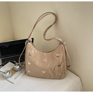 Detail of metallic beige tote bag featuring silver butterfly charms and glossy texture