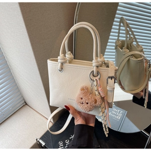 Detail of cream white pleated bucket bag with plush bear charm and woven tassel