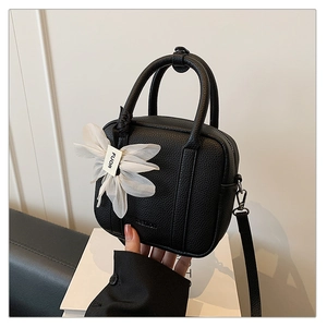Detail of black pebbled leather Boston bag with decorative white tulle flower and logo