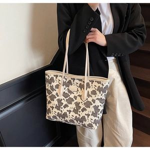 Detail of a cow print tote bag with leather handles and rectangular logo on a model