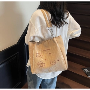 Detail der beigen Falten-Tote-Bag mit Katzenstickerei und Metallkettenriemen auf Treppen