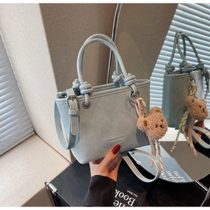 Detail of light blue bucket bag with pleated texture and plush bear charm on a black shelf