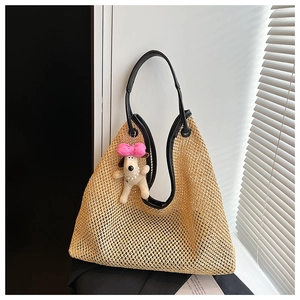 Detailed view of beige hollow straw tote bag with black leather handles and plush charm