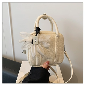 Detail of cream Boston bag with lychee grain texture and white mesh flower charm