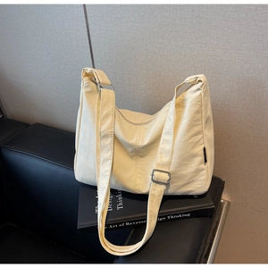 Macro view of cream-colored canvas dumpling bag with adjustable strap on a sofa
