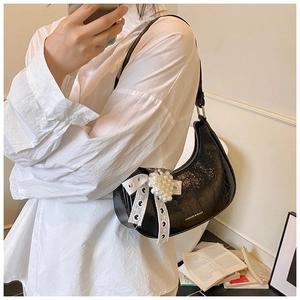 Detail of black glossy shoulder bag with lace bow, pearl heart and zip closure