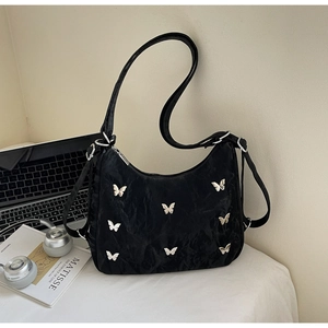 Close-up of black pleated hobo bag with silver butterfly charms in a modern desk setting