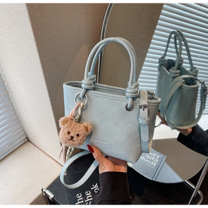 Detail of light blue pleated handbag with plush bear charm and rolled handle
