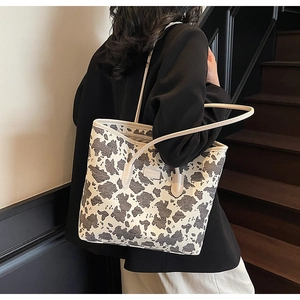 Detail of a large canvas tote bag with cow print pattern paired with a black blazer