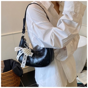 Detail of black crescent shoulder bag with crocodile texture and lace bow charm