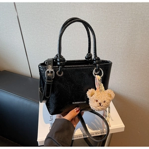 Detail of glossy pleated bucket bag featuring metallic texture and bear charm