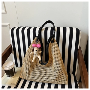Detail of handwoven straw tote bag with black leather straps and a plush puppy charm
