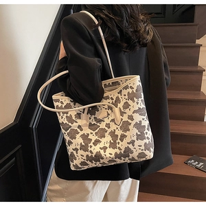 Close-up of a large cow print tote bag with thin beige straps worn on the shoulder