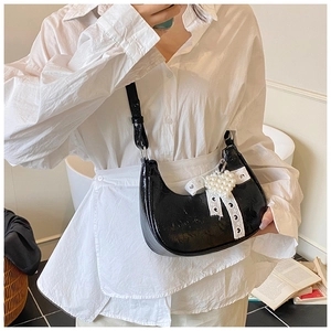 Detail of black patent leather half-moon bag with lace trim and pearl heart charm
