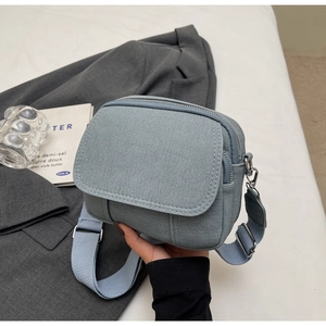 Detail van lichtblauwe canvas crossbodytas met geweven textuur en verstelbare riem