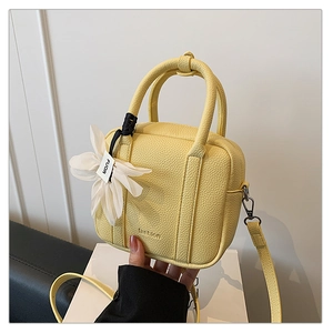 Detailed macro view of yellow lychee grain leather pillow bag with floral charm accessory