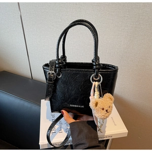Detail of black patent leather bucket bag with wrinkled texture and plush bear charm
