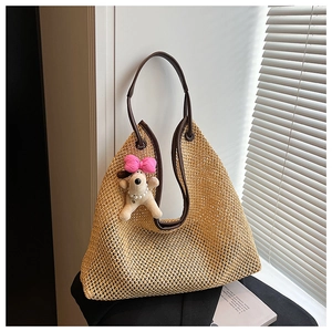 Detail shot of woven straw tote bag with brown leather handles and plush dog charm