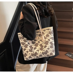 Side view of large cow print tote bag worn on shoulder by model on wooden stairs