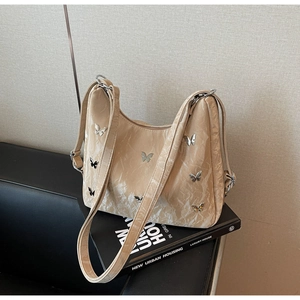 Detail of a beige pleated leather bag featuring metallic silver butterfly charms on top of a book