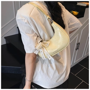 Detailed view of yellow half-moon bag with lace bows and pearl accents on shiny leather