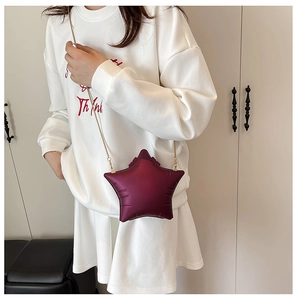 Detail of burgundy star-shaped crossbody bag featuring fine gold metal chain strap