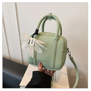 Close-up of mint green pebble leather Boston bag with floral charm and fashion logo