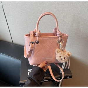 Detail of light pink tote bag with pleated faux leather texture and a bear charm