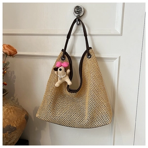 Detail of hand-woven straw tote bag with brown leather trim and cute dog charm pendant