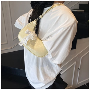 Detail of pale yellow hobo bag with pearl chain and lace bow on a textured surface